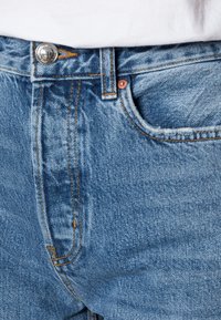 Ljust blå denimjeans med en slät yta, med koppardetaljer, kontrasterande sömmar och en klassisk femfickdesign.