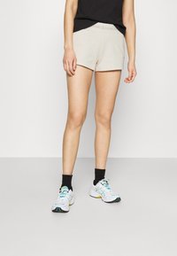 Béžové bavlněné šortky s elastickým pasem a logem Calvin Klein. V kombinaci s černými kotníkovými ponožkami a barevnými sportovními botami.