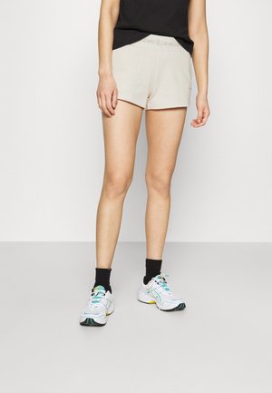 Shorts en coton beige avec une ceinture élastique et le logo Calvin Klein. Associés à des chaussettes noires jusqu'à la cheville et des chaussures de sport colorées.