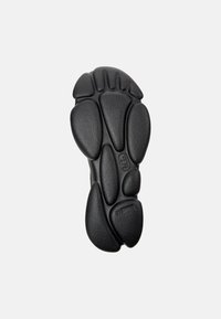 Schwarze Gummisohle mit definierten strukturierten Profilen, einem gepolsterten Design mit abgerundeten Formen und prägierten Logodetails für Griffigkeit und Stil.