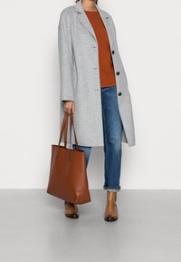 Gray wool coat with black buttons, a rust-colored knit sweater, blue jeans, brown leather ankle boots, and a brown tote bag.