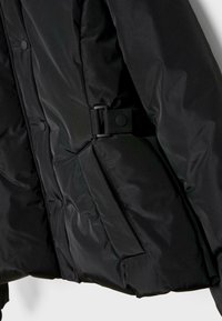 Crna pufasta jakna z zadrgo, gumbi za zapiranje in pasom. Narejena iz gladkega, sijočega materiala s podloženo teksturo.