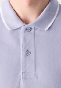 Gros plan d'un polo bleu clair avec deux boutons fermés et un col avec une bordure blanche.