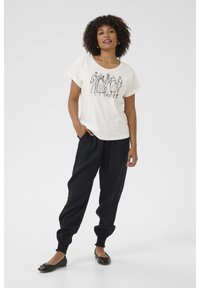 T-shirt crème à manches courtes avec un dessin de figures en ligne noire. Associé à un pantalon noir ample avec des poignets élastiques et des chaussures noires plates.