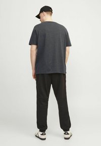 Korte mouwen, donkergrijs t-shirt gecombineerd met zwarte broeken en instapsandalen. De outfit heeft een ontspannen pasvorm en minimale details.