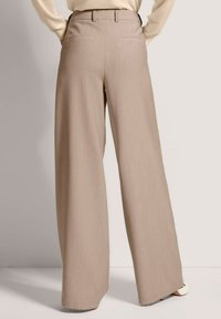 Breiwijdige beige broek met een zachte textuur, voorzien van een hoge tailleband en achterzakken. Strakke lijnen zonder patronen of hardware details.