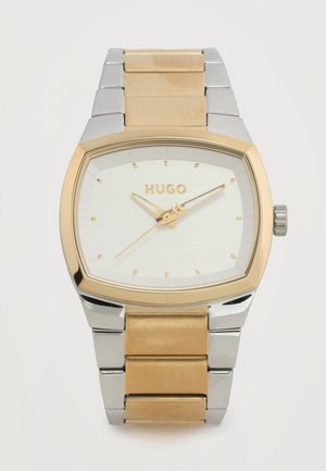 Vyriškas Hugo riešo laikrodis su stačiakampiu aukso ir sidabro spalvos nerūdijančio plieno dirželiu bei baltu ciferblatu su aukso spalvos rodyklėmis ir žymėmis.