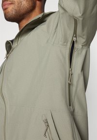 Lightweight, olive green jacket with a grid pattern, featuring zippered pockets, adjustable cuffs, and a zip closure. Textured fabric.