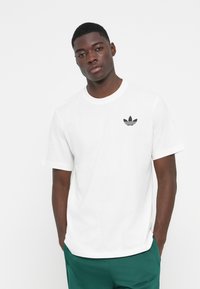 Hvid bomulds t-shirt med korte ærmer og rund halsudskæring, med et sort Adidas trefoil-logo på venstre bryst.