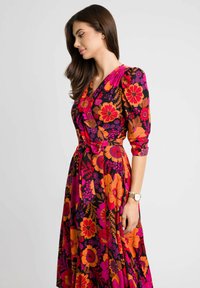 Sukienka w kwiaty w kolorze czarnym z intensywnymi pomarańczowymi, różowymi i fioletowymi kwiatami. Posiada pasek, rękawy o długości trzech czwartek oraz płynny krój.