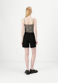 Camisola s uzorkom leoparda s tankim naramenicama, u kombinaciji s crnim šortsevima visokog struka. Donji dio ima dva stražnja džepa i ležeran kroj.