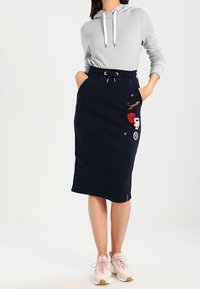 Falda navy con cintura ajustable, adornada con parches bordados y estrellas. Combinada con una sudadera gris y zapatillas de color rosa claro.