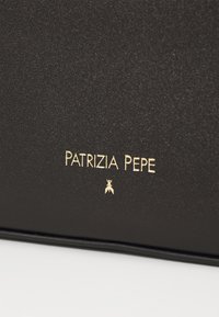 Superficie nera testurizzata con testo dorato in rilievo "PATRIZIA PEPE" e un piccolo logo sottostante. Design elegante e minimalista.