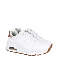 Zapatillas Skechers blancas con detalles en tono beige, con perforaciones, suelas acolchadas y bolsas de aire visibles sobre un fondo blanco.