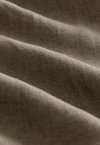 Linnedug i en dæmpet brun farve. Blød tekstur med synlige vævemønstre og blid drapering, der fremhæver dens naturlige fibre.