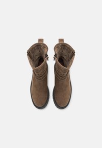 Bottines en daim marron à bout arrondi, avec une fermeture éclair sur le côté et une semelle en caoutchouc noir texturé. Intérieur en laine polaire, doublure douce.