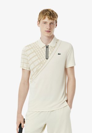Polo en crème avec un motif quadrillé beige texturé et une fermeture éclair noire. Présente un logo vert sur la poitrine et des manches courtes.