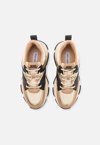 Sneaker beige e neri con un design chunky, realizzati in materiali sintetici, con lacci, una linguetta sul tallone e un logo di marca ben in vista.