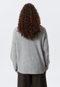 Pull en tricot gris à la coupe décontractée, avec un ourlet côtelé et des manches longues. Texture douce et design simple avec un col rond.