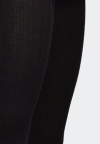 Detailní záběr na černou žebrovanou texturu látky na zakřiveném povrchu, který zdůrazňuje jemný vertikální pletený vzor a decentní stíny.