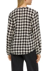 Langsleeve blouse met een houndstooth patroon in zwart en crème, met een ronde halslijn en elastische mouwen.