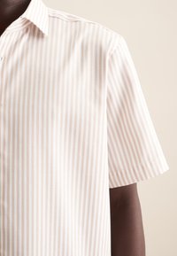 Camicia a maniche corte di un beige chiaro con righe bianche verticali. Presenta un colletto a punta e una texture liscia con una vestibilità slim.