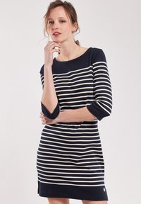 Robe rayée bleu marine et blanche avec des manches trois-quarts, un col rond et des fentes sur les côtés. Tissu doux avec un léger stretch et un branding minimal.