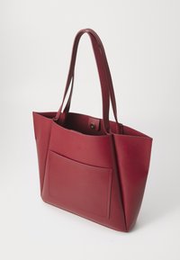 Rød skinn tote bag med to håndtak, flat bunn og en ytterslomme. Glatt tekstur med rene linjer og ingen synlig maskinvare.