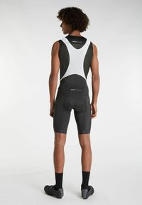 Čierne cyklistické kraťasy s textúrovaným dizajnom, obsahujúce bielu sieťovú hornú časť a vystlané sedlo. Model nosí tmavé cyklistické topánky a ponožky.