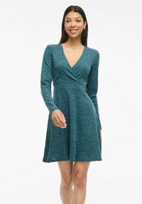 Teal wrap dress with long sleeves, textured pattern, fitted waist, and flared skirt. Made from a soft, stretchy fabric.