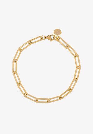 Arm einer Frau, die ein zartes goldenes Armband trägt, neben einem olivgrünen plissierten Kleid mit geraffter Taillendetail.