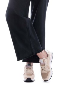 Zapatillas beige de materiales de ante y malla. Cuentan con cierre de cordones, una suela acolchada y un detalle en blanco y rosa en el talón. Se pueden ver jeans negros de pierna ancha.