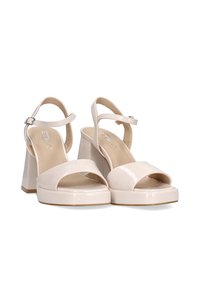 Sandalias de plataforma de charol beige con puntera abierta, correa en el tobillo y tacón cuadrado. Textura suave con un acabado brillante.