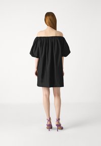 Svart off-the-shoulder kjole med pufferm, med en samlet halslinje og en løs silhuett. Brukt med lilla hæler med stropper.