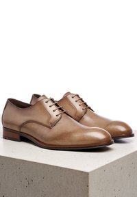 Bruine leren veterschoenen met een gladde afwerking, ronde neus en minimalistisch ontwerp. Voorzien van een houten hak en subtiele zijnaden.