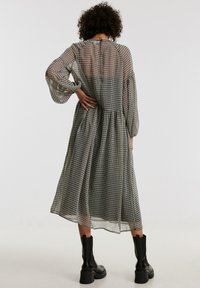 Schwarz-weißer karierter Midikleid mit langen transparierenden Ärmeln, geraffter Taille und einem fließenden Rock. Kombiniert mit schwarzen Knöchelstiefeln.
