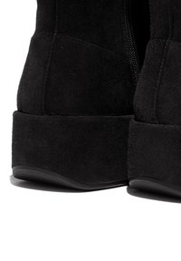 Zwarte suède enkellaarsjes met een gestructureerde afwerking, voorzien van een ritsdetail en een iets verhoogde rubberen zool voor extra hoogte.