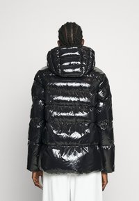 Czarna kurtka puchowa z połyskującym wykończeniem, z kapturem i pikowanym wzorem, widocznymi poziomymi szwami oraz elastycznymi mankietami.