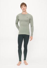 Langermet topp i dempet olivengrønn stoff, kombinert med mørke leggings med ombre-tekstur fra mørkegrønn til lys.