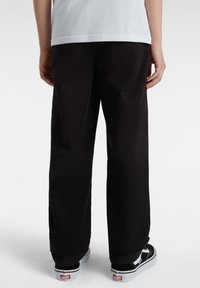 Zwarte wijde broek van textuurstof, met een gladde tailleband en zakken. Gemonteerd met zwart-witte Vans schoenen.