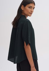 Dark green, ribbed blouse with short sleeves and a high neck. Features a relaxed fit and side slits. Textured fabric adds depth.