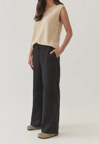 Beige ärmlös topp i strukturerad stickning, kombinerad med löst sittande, mörkgrå linbyxor och taupe slip-on skor.