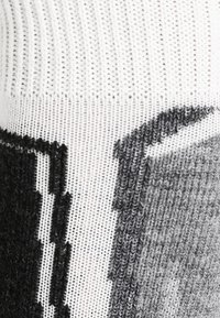 Jersey de punto con un cuello blanco acanalado, que presenta un patrón gráfico pixelado en negro y gris. Textura suave y diseño ajustado.