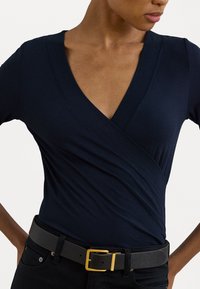Navy blue wrap top made of soft fabric with a V-neck design. Paired with a black belt featuring a gold buckle, textured strap, and silver hardware.