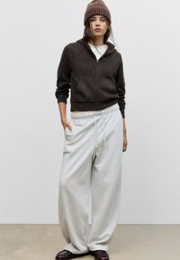 Brązowy sweter z zamkiem błyskawicznym, krótki, szare luźne spodnie dresowe, brązowa i kremowa czapka, warstwowy biały top, fakturowany materiał, luźny krój.