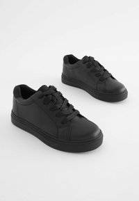 Baskets noires en cuir synthétique avec un design bas, bout rond, lacets à l'avant, et semelles en caoutchouc texturé pour une meilleure adhérence.