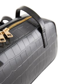 Czarna skórzana torebka z teksturą krokodyla, złotym podwójnym zamkiem błyskawicznym i górnymi uchwytami, ukazana z bliska pod kątem na białym tle.