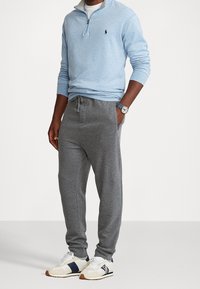 Ljusblå zip-neck-tröja, grå sweatpants med dragsko, och beige sneakers med marinblå accenter. Tröjan har en liten logotyp.