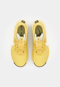 Chaussures d'entraînement Nike en jaune vif, avec un dessus en mesh, un swoosh blanc contrastant et une semelle en caoutchouc texturé pour une meilleure adhérence.