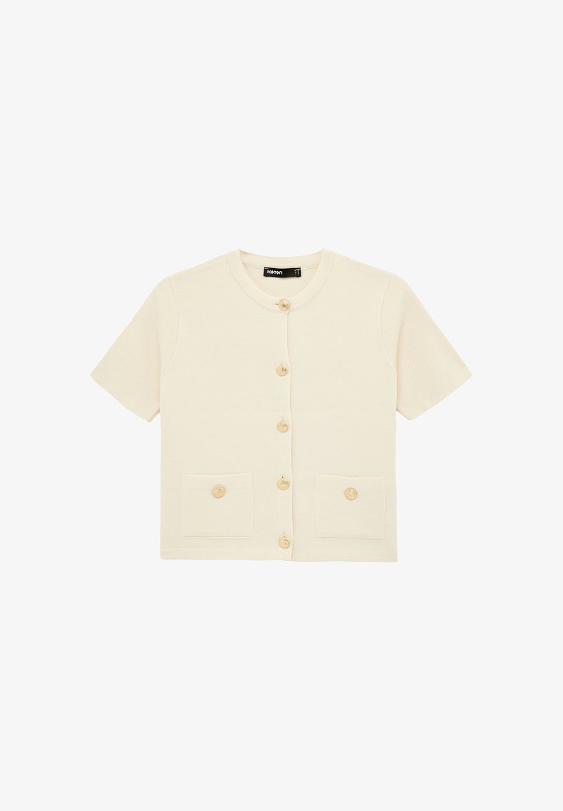 Kortærmet cremefarvet cardigan med rund halsudskæring, knapper foran og to knap-lukkede forlommer, lagt fladt på hvid baggrund.